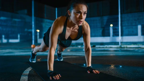 Gyönyörű Sportos Fitness Girl csinál push up gyakorlatok. Edzést tart egy bekerített szabadtéri kosárlabdapályán. Éjszakai felvételek esőzés után egy lakóövezetben. — Stock Fotó