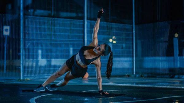 Bella ragazza di fitness sportiva che fa esercizi push up. Sta facendo un allenamento in un campo da basket all'aperto recintato. Notte dopo la pioggia in una zona residenziale. — Foto Stock