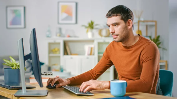 Retrato de un joven guapo trabajando en una computadora personal desde casa. En acogedor brillante sala de estar Hombre navega a través de Internet. — Foto de Stock