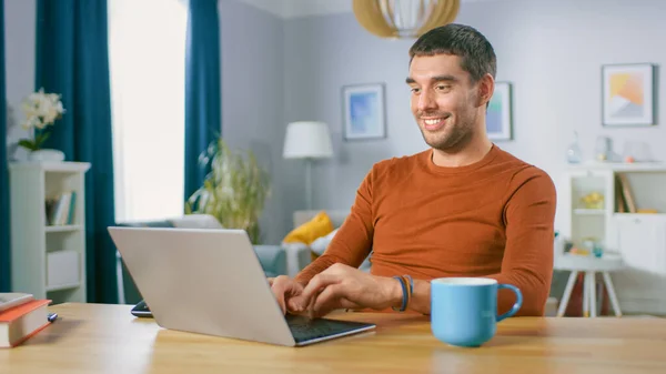 Πορτραίτο του όμορφου χαμογελαστού ανθρώπου που εργάζεται σε φορητό υπολογιστή, κάθεται στο ξύλινο γραφείο του στο σπίτι. Ο άνθρωπος που περιηγείται στο Διαδίκτυο, που εργάζονται σε σημειωματάριο από το σαλόνι του. — Φωτογραφία Αρχείου