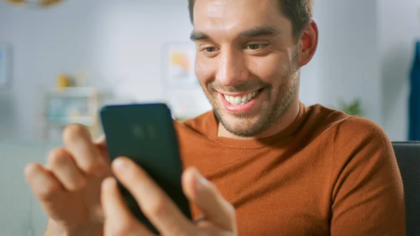 Evdeki Yakışıklı Heyecanlı Mutlu Adam Akıllı Telefon Kullanıyor. Oturma odasında cep telefonuyla rahatlayan bir adam.. — Stok fotoğraf