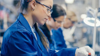 Mavi İş Ceketi ve Koruyucu Gözlüklü Kadın Elektronik Fabrikası İşçisi, dizüstü bilgisayarları tornavidayla monte ediyor. Çoklu Çalışanlarla Yüksek Teknoloji Fabrikası.