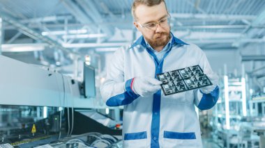 Yüksek Teknoloji Fabrikası: Kalite Kontrol Müfettişi Elektronik Yazılı Devre Panosunu Hasar Kontrol Ediyor. Yüzey Mount Pick ve Place Technology ile PCB için Arkaplan Assembly Line 'da.