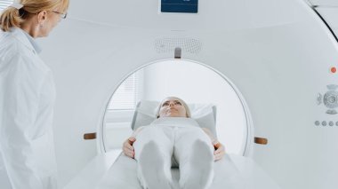 Tomografide veya MRI taramasında yatan bir kadının yakın plan portresi. Yatak, vücudunu ve beynini tararken makinenin içinde hareket ediyor. Yüksek Teknolojik Ekipmanlarla Tıbbi Laboratuvarda.