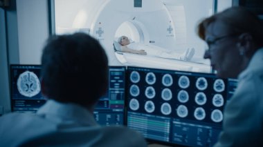 Kontrol Odası 'nda Doktor ve Radyoloji Uzmanı, İşlem ve Beyin Taraması Sonuçlarını İzlerken Tanıyı Tartışıyor, Arka plandaki Hasta MRI veya CT Tarama İşleminden Geçiyor.