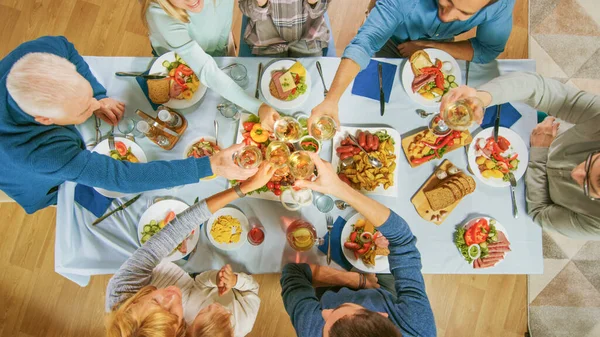 Große Familien- und Freundesfeier zu Hause, vielfältige Menschentrauben am Tisch, Gläserklirren beim Toast. Menschen essen, trinken und haben Spaß im Wohnzimmer. Top-Down-Schuss. — Stockfoto