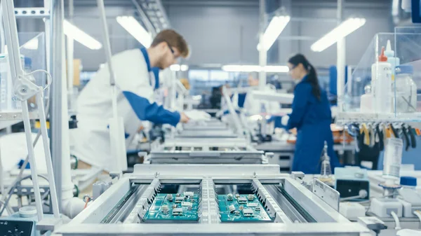 Disparo de una fábrica de electrónica Los trabajadores ensamblan placas de circuitos a mano mientras se encuentra en la línea de montaje. Instalación de fábrica de alta tecnología. —  Fotos de Stock