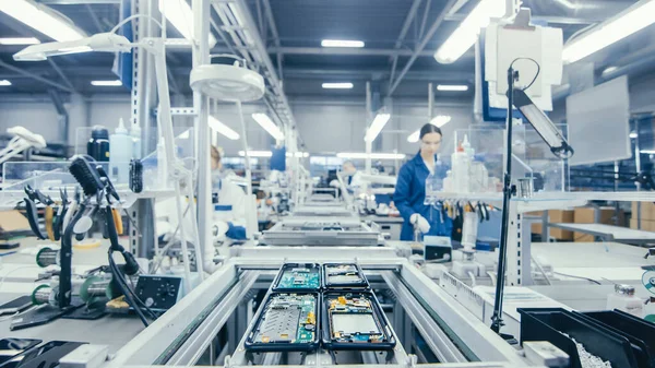 Disparo de una fábrica de electrónica Los trabajadores ensamblan placas de circuitos a mano mientras se encuentra en la línea de montaje. Instalación de fábrica de alta tecnología. — Foto de Stock