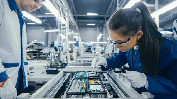 Disparo de una fábrica de electrónica Los trabajadores ensamblan placas de circuitos a mano mientras se encuentra en la línea de montaje. Instalación de fábrica de alta tecnología. — Foto de Stock