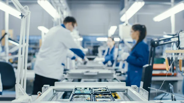 Shot of an Electronics Factory Workers Assembling Circuit Boards by Hand While it Stands on the Assembly Line. High Tech Factory Facility.