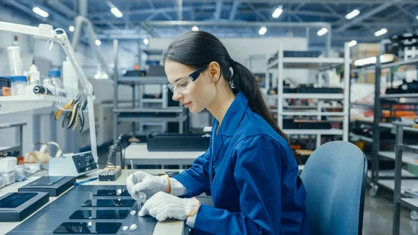 Ung kvinna i blått arbete Coat är att montera tryckta kretskort för smartphones. Fabriksanställda inom elektronik i en fabrik för högteknologi. — Stockfoto
