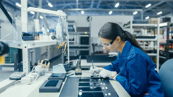 Jovem fêmea em Blue Work Coat está montando placas de circuito impresso para smartphones. Fábrica de eletrônicos Trabalhadores em uma instalação de fábrica de alta tecnologia. — Fotografia de Stock