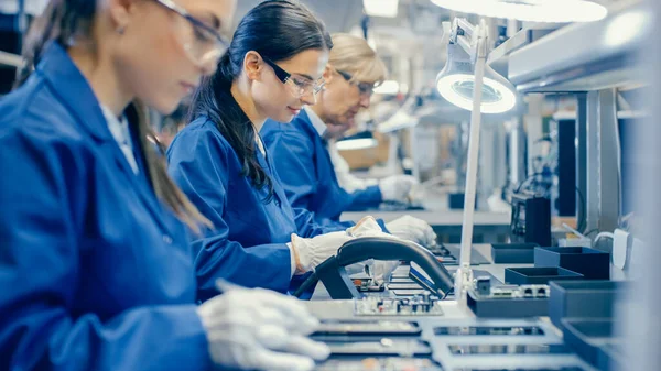 Arbeiterinnen der Elektronikfabrik in blauem Arbeitsmantel und Schutzbrille montieren mit Pinzette Leiterplatten für Smartphones. High-Tech-Fabrik mit Mitarbeitern. — Stockfoto