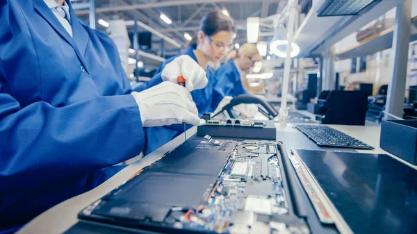 Detailní záběr pracovnice továrny na elektroniku v modrém pracovním plášti Montáž notebooků Motherboard se šroubovákem. Zařízení High Tech Factory s více zaměstnanci. — Stock fotografie