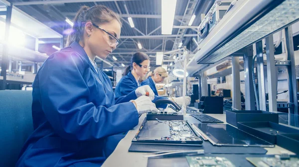 Woman Electronics Factory Εργάτης σε μπλε παλτό εργασίας και προστατευτικά γυαλιά συναρμολογεί φορητούς υπολογιστές Μητρική πλακέτα με ένα κατσαβίδι. Εγκαταστάσεις υψηλής τεχνολογίας με πολλαπλούς υπαλλήλους. — Φωτογραφία Αρχείου