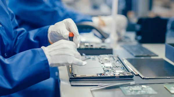 Close-Up of a Female Electronics Factory Worker in Blue Work Coat Assembling Laptops Motherboard with a Screwdriver. Fábrica de alta tecnología con múltiples empleados. — Foto de Stock