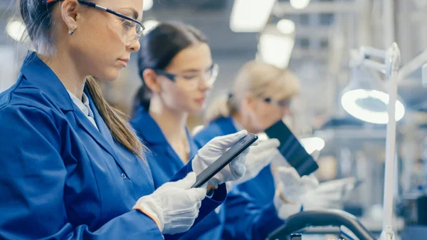ブルーワークコートと保護メガネの女性電子工場労働者は、スマートフォンの画面を取り、品質チェックを実行します。従業員数の多いハイテク工場. — ストック写真
