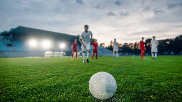 スタジアムの芝生の上に横たわるサッカーボールのショット。プロサッカー選手は相手チームのメンバーを追放し、ゴールを決めるためにボールをキックする準備ができている. — ストック写真