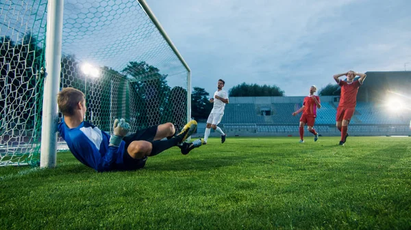 スタジアムの攻撃者がボールを蹴ってゴールを決めると、サッカーのゴールキーパーはゴールを守ろうとしますが、ジャンプしてボールをキャッチできません. — ストック写真