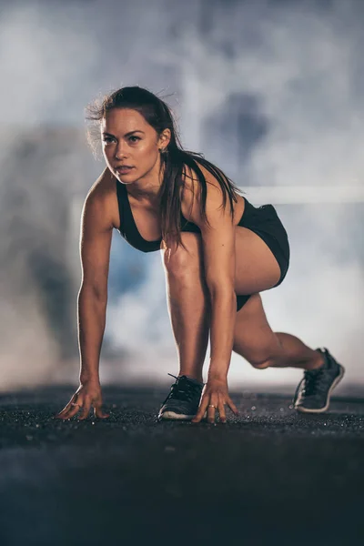 Девушка в черном спортивном топе и с вытянутыми ногами для бега. Она в городской среде под мостом с туманным прошлым. — стоковое фото