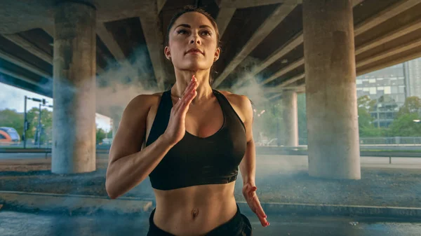 Close Up Portrait Shot of a Beautiful Confident Fitness Girl in Black Athletic Top and Shorts Jogging Through a Foggy Street (em inglês). Ela está correndo em um ambiente urbano sob uma ponte com carros no — Fotografia de Stock