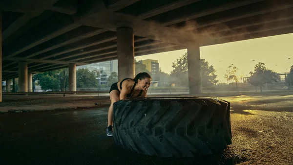 Schöne selbstbewusste Fitness-Mädchen in schwarzem athletischen Top macht Übungen auf der Straße. Shops versuchen, große schwere Reifen in einer städtischen Umgebung zu heben. — Stockfoto