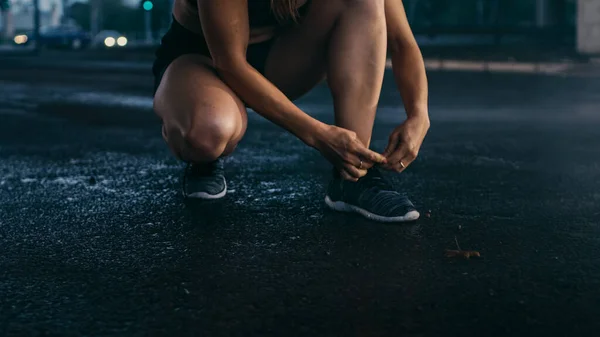 美しい自信のフィットネスガールのクローズアップショットは、靴ひもを結びます.彼女は背景に車と橋の下の都市環境にある. — ストック写真