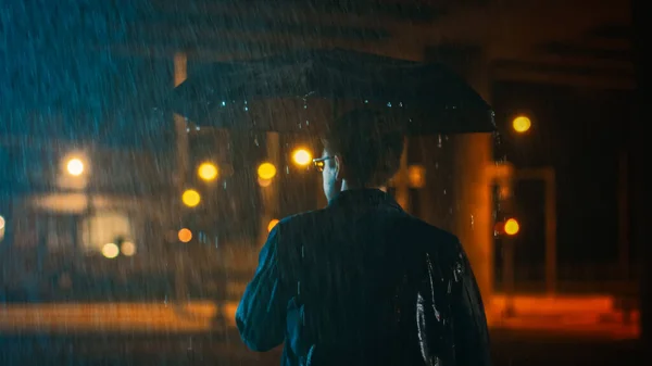 Backshot of a Young Caucasian Shorthaired Man, Wearing a Jeans Coat Walking in the Rain Under an Umbrella. Hes Walking at Night in the City. — Stock Photo, Image