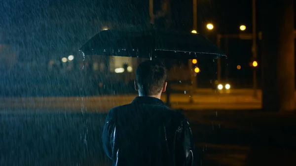 Backshot of a Young Caucasian Shorthaired Man, Wearing a Jeans Coat Walking in the Rain Under an Umbrella (em inglês). Caminhando à noite na cidade. — Fotografia de Stock