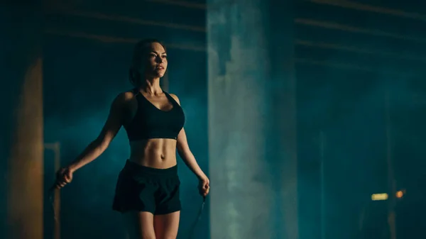 Beautiful Energetic Fitness Girl in Black Athletic Top and Shorts είναι παραλείποντας Jumping Rope. Κάνει μια προπόνηση σε ένα απογευματινό ομιχλώδες αστικό περιβάλλον κάτω από μια γέφυρα. — Φωτογραφία Αρχείου