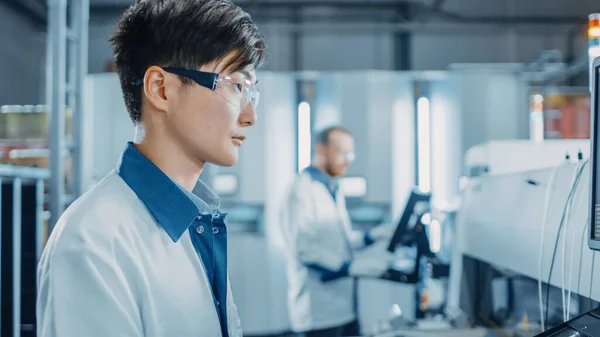 Portrait Shot of an Asian Engineer in High Tech Factory utiliza la computadora para programar Pick and Place Electronic Machinery for Printed Circuit Board Assembly Line. Producción de PCB con SM Machinery. — Foto de Stock