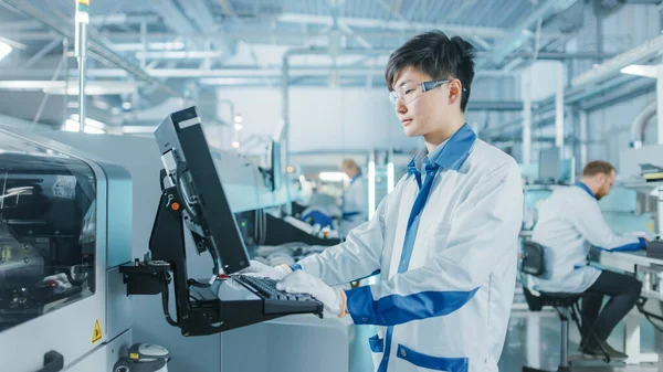 En la fábrica de alta tecnología, el ingeniero asiático utiliza una computadora para programar la selección y colocar maquinaria electrónica para la línea de ensamblaje de montaje en superficie de placa de circuito impreso. Producción de PCB con maquinaria SMT. — Foto de Stock