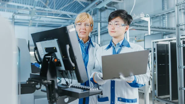 On High Tech Factory Asian Engineer Talks with Female Supervisor, Use Computer for Programming Pick and Place Electronic Machinery for Printed Circuit Board Surface Mount Assembly Line. Výroba: — Stock fotografie