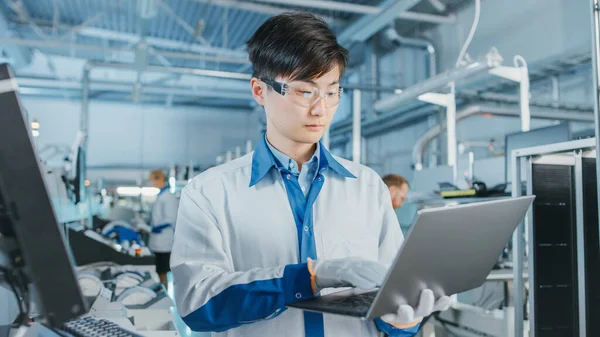 On High-Tech Factory Asian Engineer uses Laptop Computer for Programing Pick and Place Electronic Machinery for Printed Circuit Board Surface Mount Line. Výroba desek s SMT strojem. — Stock fotografie