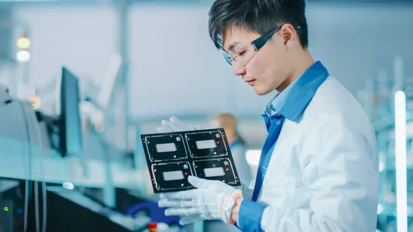 High-Tech Factory: Quality Control Engineer controleert Electronic Printed Circuit Board het voor schade. In de achtergrond assemblagelijn voor printplaat met oppervlaktemontage Pick and Place Technology. — Stockfoto