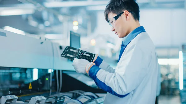 High-Tech Factory: Kvalitetskontroll Ingenjör kontrollerar elektroniska tryckta kretskort det för skador. I bakgrundsmonteringslinjen för PCB med utanpåliggande fäste Pick and Place Technology. — Stockfoto