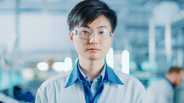 2011 년 4 월 1 일에 확인 함 . On High-Tech Factory: Portrait of Asian Worker Wearing Uniform and Safety Goggles.. 배경에 흐릿 한 전자 조립 라인에서 브라이트 라이트 및 다른 근로자들이 그들의 직업을 수행하는 모습. — 스톡 사진
