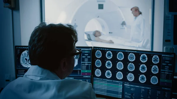 Orvosi laborban a beteget MRI vagy CT vizsgálatnak vetik alá radiológus felügyelete mellett, az irányítóteremben Orvosórák eljárása és az agyműködés monitorozása mellett.. — Stock Fotó