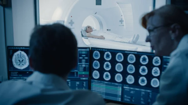 The Control Room Dr. and Radiologist Discuss Diagnosis during Watching Procedure and Monitors show Brain Scans Results, In the Background Patient Undergoes MRI or CT Scan Procedure. — 스톡 사진