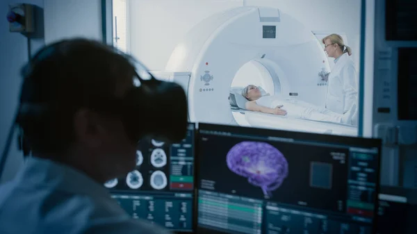 Conceito Futurista: Na Sala de Controle Médico Médico Usar Headset de Realidade Virtual Monitora Paciente Submetido a RM ou TC Procedimento de Digitalização. Exibe o modelo 3D do cérebro da mostra do computador com câncer possível. — Fotografia de Stock