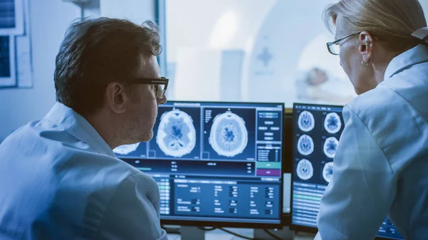 対照室で医師と放射線科医は、脳スキャンの結果を示す手順やモニターを見ながら診断について話し合います,背景にある患者は、 MRIやCTスキャンの手順を受けます. — ストック写真