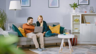 Mutlu Mutlu Çift Evdeki Koltukta Oturuyor, Erkek Arkadaş Dizüstü bilgisayarını dizlerinde tutuyor, interneti tarıyor, e-alışveriş yapıyor, Akış Hizmetlerini kullanıyor. Mutlu Aile Oturma Odasında.