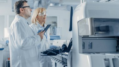 Tablet Bilgisayarlı İki Araştırma Bilimadamı Program Tıbbi Ekipmanı. Modern Laboratuvarda Tıbbi Araştırma Yapan Profesyoneller Ekibi.