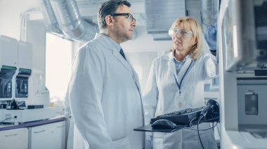İki Araştırmacı Bilim Adamı Testler için Tıbbi Ekipman Programlama hakkında konuşuyor. Modern Laboratuvarda Tıbbi Araştırma Yapan Profesyoneller Ekibi