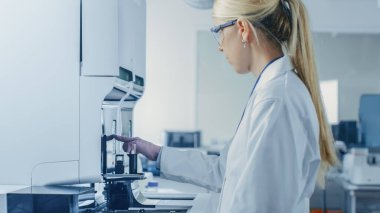 Kadın araştırmacı test tüpünü kan örneğiyle Tıbbi Analiz Ekipmanına yerleştirdi. Modern İlaç Laboratuvarında Bilim Adamı Çalışıyor.