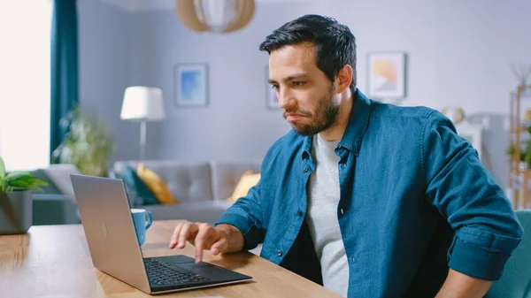 Πορτρέτο του Όμορφου Νέου Χρησιμοποιώντας Laptop Computer στο σπίτι, Κάνοντας μια θλιβερή πρόσωπο και να μετανιώσετε για την απώλειά του. Άνετο μοντέρνο επίπεδο γίνεται σε σκανδιναβικό στυλ. — Φωτογραφία Αρχείου