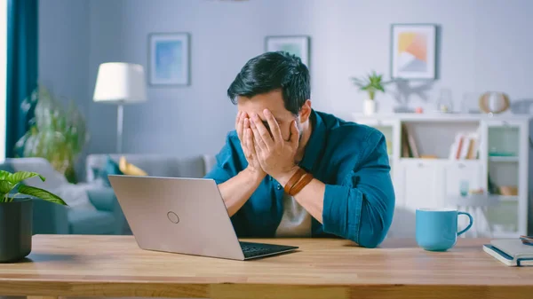 Shot of an Upset Young Man Covers His Face with Palms in Frustration, terwijl het krijgen van slecht nieuws uit het lezen van slecht nieuws op een laptop. Verontruste man thuis. — Stockfoto