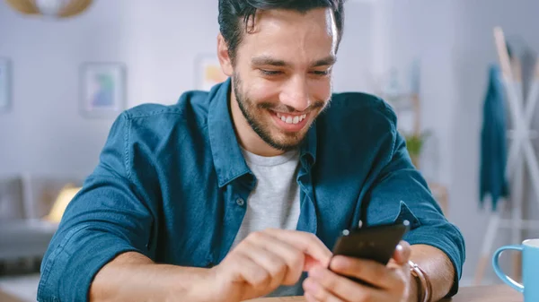 Yakışıklı Gülümseyen Adam Salonunda dinlenirken Akıllı Telefon kullanıyor. Guy internette geziniyor, sosyal ağları kullanıyor, evde eğleniyor.. — Stok fotoğraf