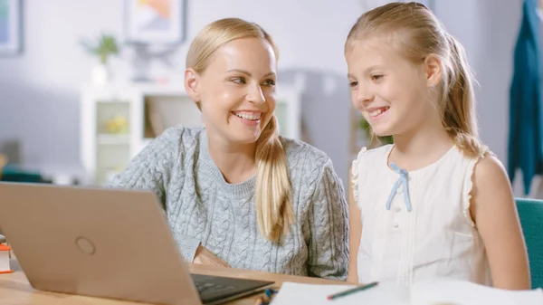 Helder meisje studies met haar mooie jonge moeder studie school lessen thuis. Toegewijde moeder helpt haar slimme dochter huiswerk te maken. Ze gebruiken Laptop.. — Stockfoto