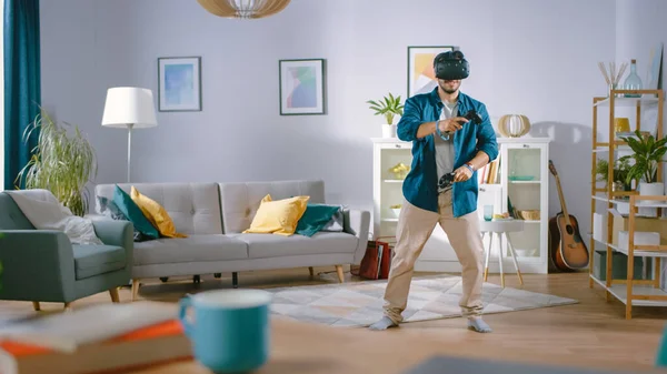 Energetico giovane uomo che indossa le cuffie di realtà virtuale e controllori Holding Gioca in un videogioco a casa. Uomo che gioca VR Shooter nel mezzo del soggiorno. — Foto Stock